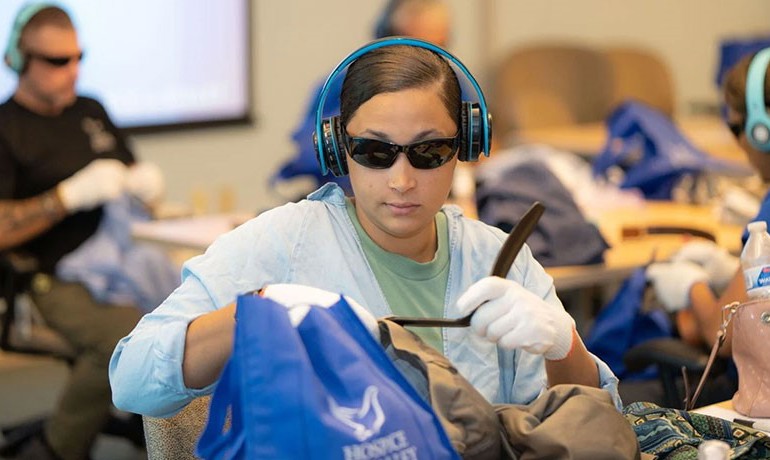 A participant attempts to complete daily tasks while wearing headphones, glasses, and gloves to simulate the dementia experience.