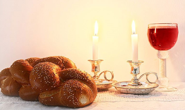 Challah bread on table with candles and goblet