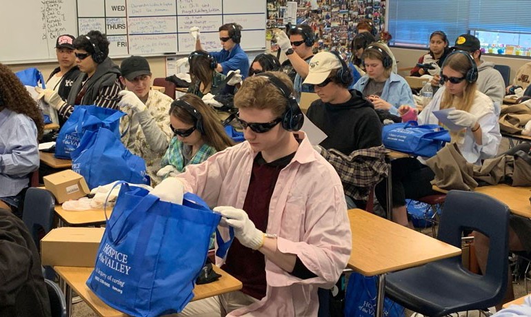 Students at desks wearing headphones, sunglasses and gloves