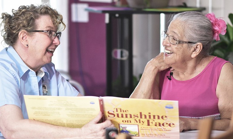 Gail Higgenbotham reads a book with patient Tomasa