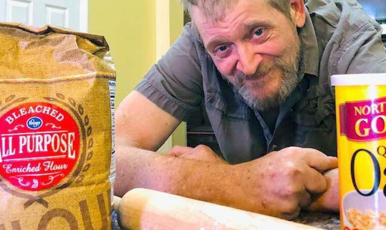 Baker leaning on counter behind bag of flour and rolling pin