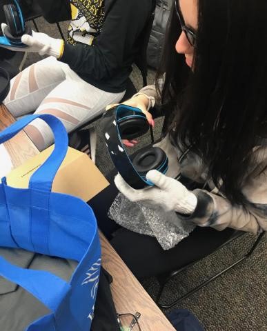 Student wearing sunglasses and gloves, and holding headphones